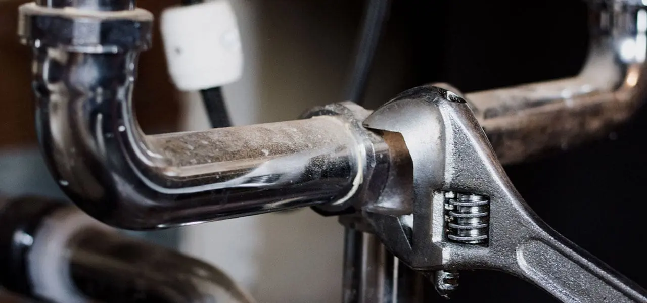 Chrome plumbing pipework being tightened with an adjustable wrench